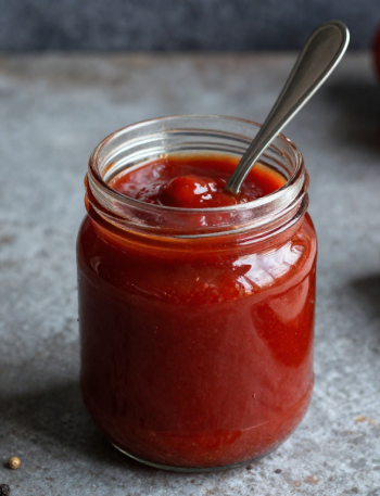 Homemade low carb keto ketchup in a jar with tomatoes in the background